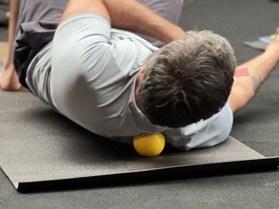 Participante deitado no tapete liberando as costas com uma bola de massagem
